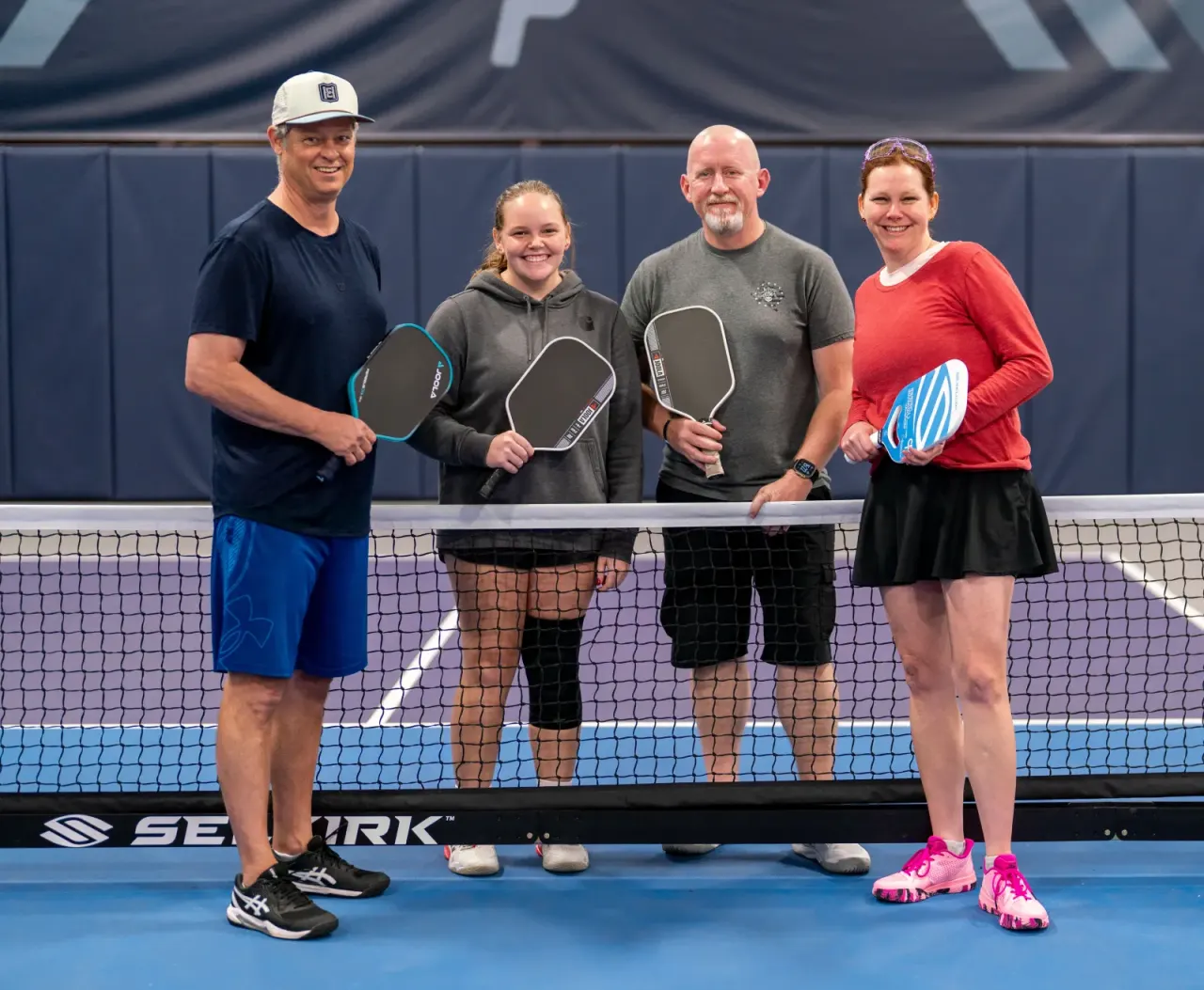 Adults gathered with paddles at the net at Pickleland