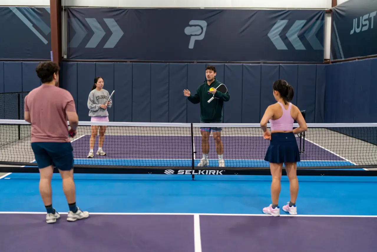 Adults playing doubles during a pickleland lesson on an indoor court