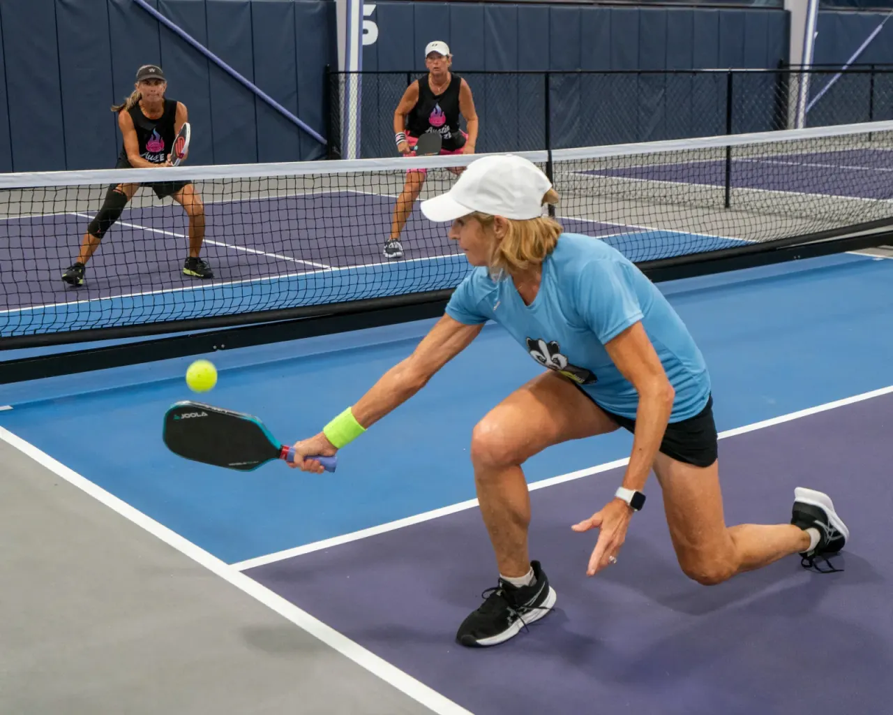 Player in a wide athletic stance making soft contact at the kitchen line — the foundation of the pickleball reset