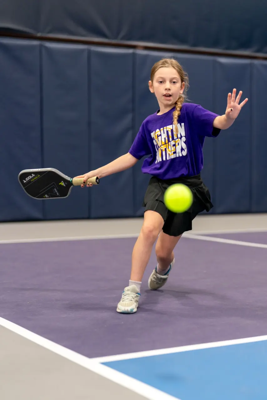 Girl in a purple shirt hits a forehand